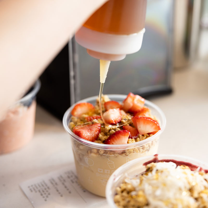Rush Bowls worker adding delicious and healthy toppings to a acai bowl meal!