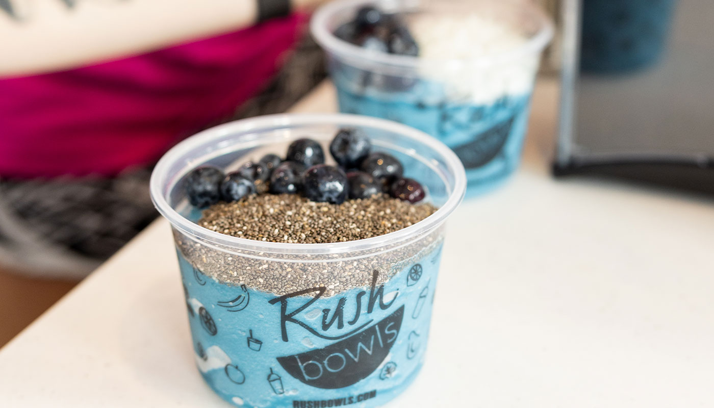 A delicious acai bowl getting taken by someone who is going to enjoy every bite of Rush Bowls's healthy meal.