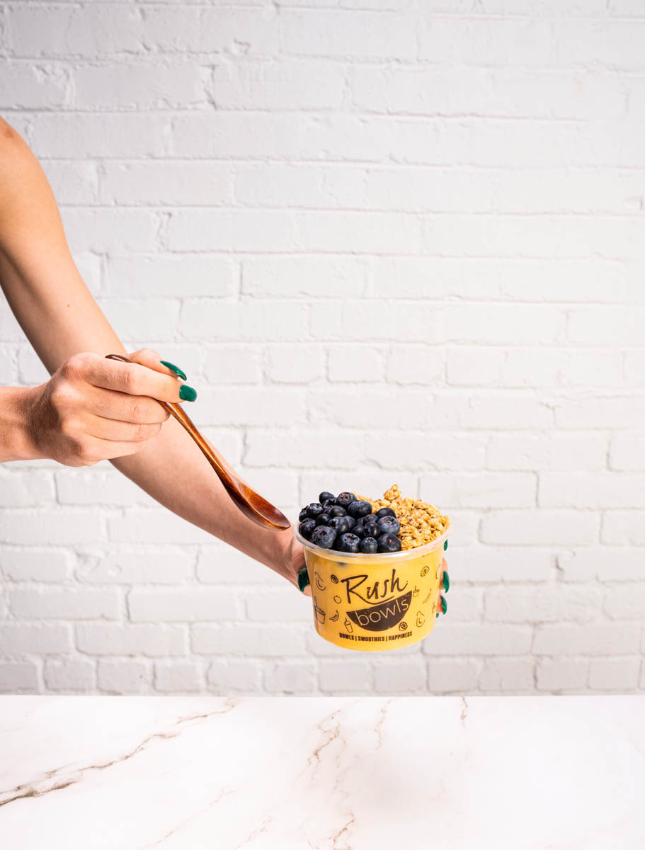 A beautifully shot fruit bowl with a white brick background  - How much does it cost to start an acai and smoothie franchise with Rush Bowls? Find out today!